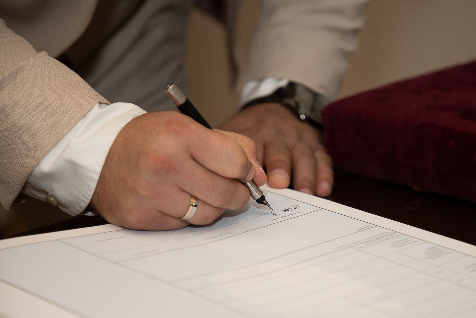 A hand signing a document with a fountain pen on a desk